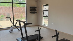 A gym with exercise equipment, large windows, and a brick wall outside.