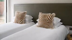 A hotel room with two beds, zebra-patterned pillows, a ceiling fan, and a window providing a view outside.