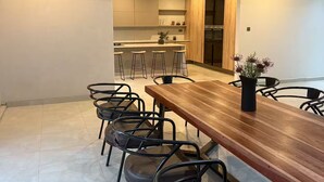 A modern dining area with a wooden table and metal chairs, a kitchen in the background, and a potted plant on the table.