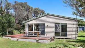 A small, single-story wooden house with a sloped roof, a front porch with a table and chairs, and a fenced yard. - The Ash, Sandy Point (Sandy Point)