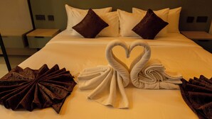 A neatly made bed with white and brown pillows, a heart-shaped towel arrangement, and a brown decorative pillow on a hotel room bed. - Emboita Hotels ltd (Nakuru)