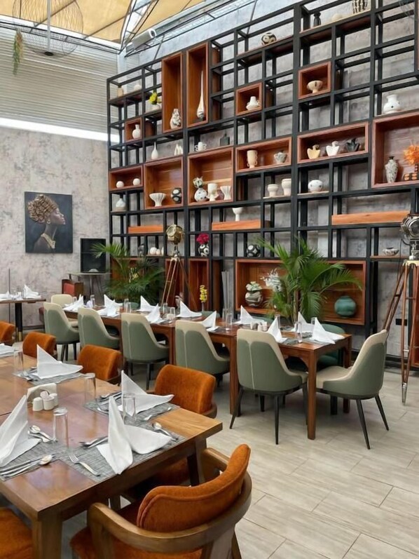 A restaurant with multiple dining tables, chairs, and a large wall of shelves with various decorative items. - Emboita Hotels ltd (Nakuru)
