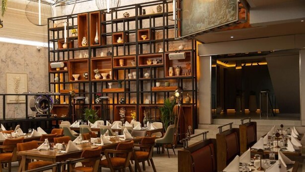 A restaurant with multiple dining tables and chairs, a large wall of shelves with various items, and a modern interior design. - Emboita Hotels ltd (Nakuru)