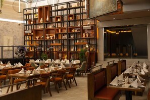 A restaurant with multiple dining tables and chairs, a large wall of shelves with various items, and a modern interior design. - Emboita Hotels ltd (Nakuru)
