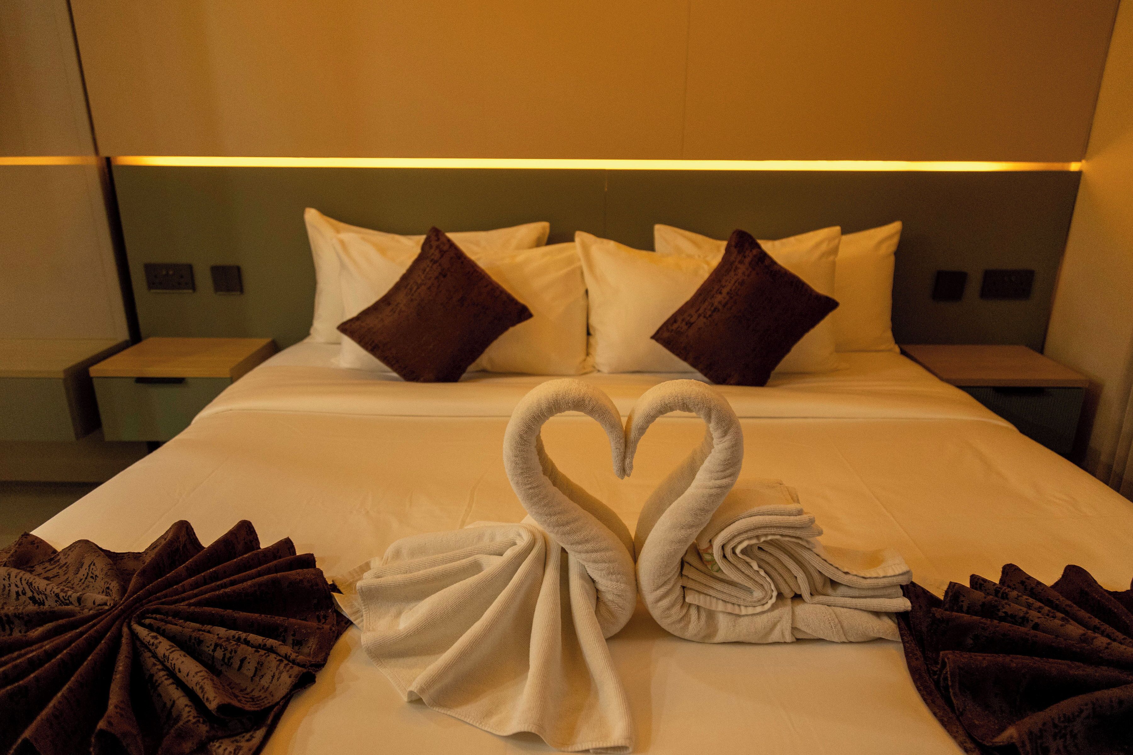 Habitación de hotel con una cama bien hecha, almohadas y toallas dispuestas en forma de corazón.