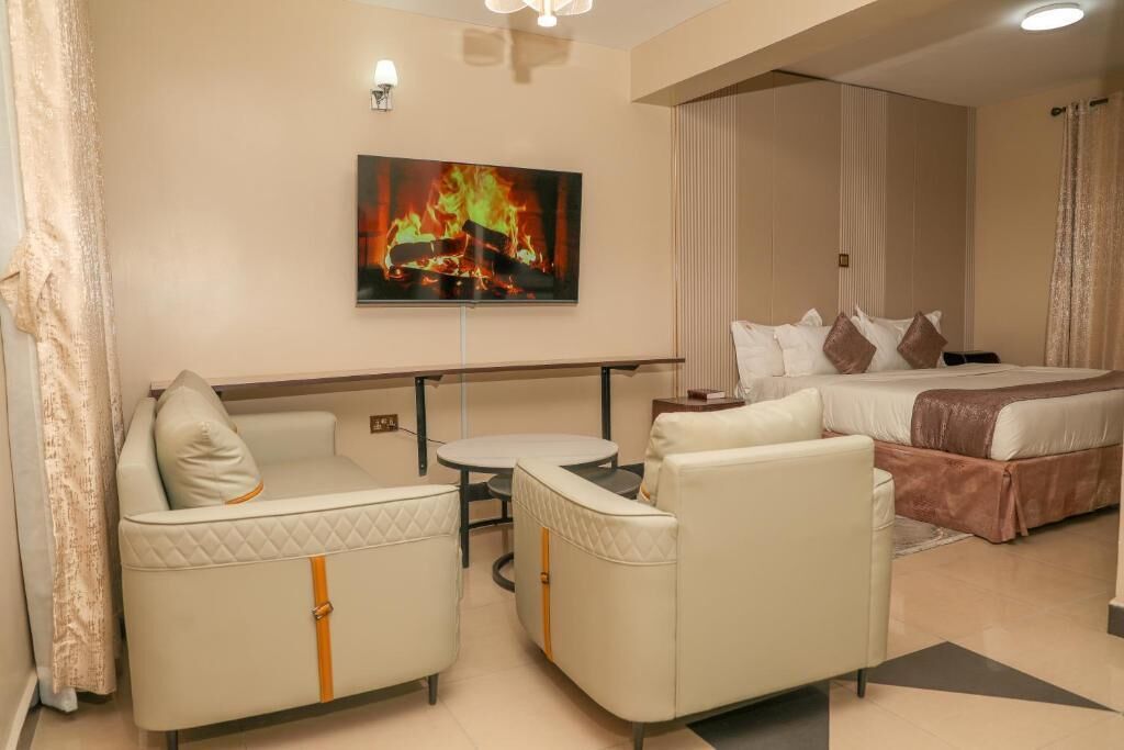 A hotel room with a bed, a sofa, a small table, and a TV displaying a fire.
