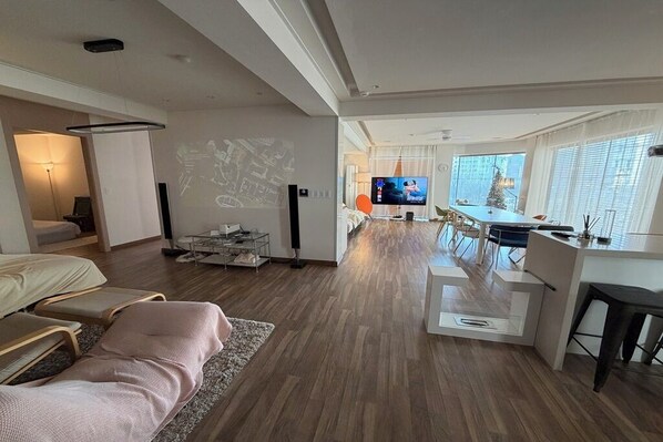 A modern living room with a sofa, a dining area with a TV, and a kitchen.