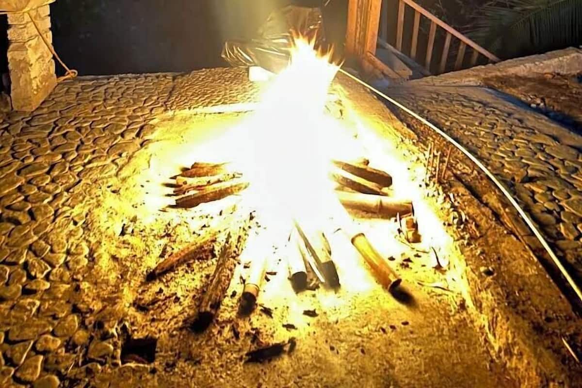 A campfire with logs arranged in a circle, surrounded by a stone-paved area with a wooden bench and a stone wall.