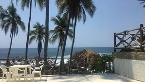 A pool area with a view of the ocean, surrounded by palm trees and a rock formation. - Cocos camp (Acapulco)