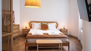Une chambre à coucher bien rangée, avec un lit, des tables de chevet, une lampe suspendue et un banc en bois.