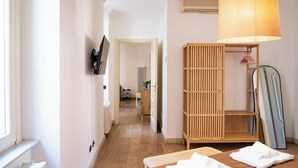 Un couloir doté d’un plancher en bois, d’un téléviseur fixé au mur, d’une armoire en bois avec une lampe suspendue et d’un miroir appuyé contre le mur.