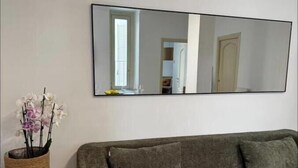 Un salon avec un canapé gris, un grand miroir et un panier en osier rempli de fleurs.