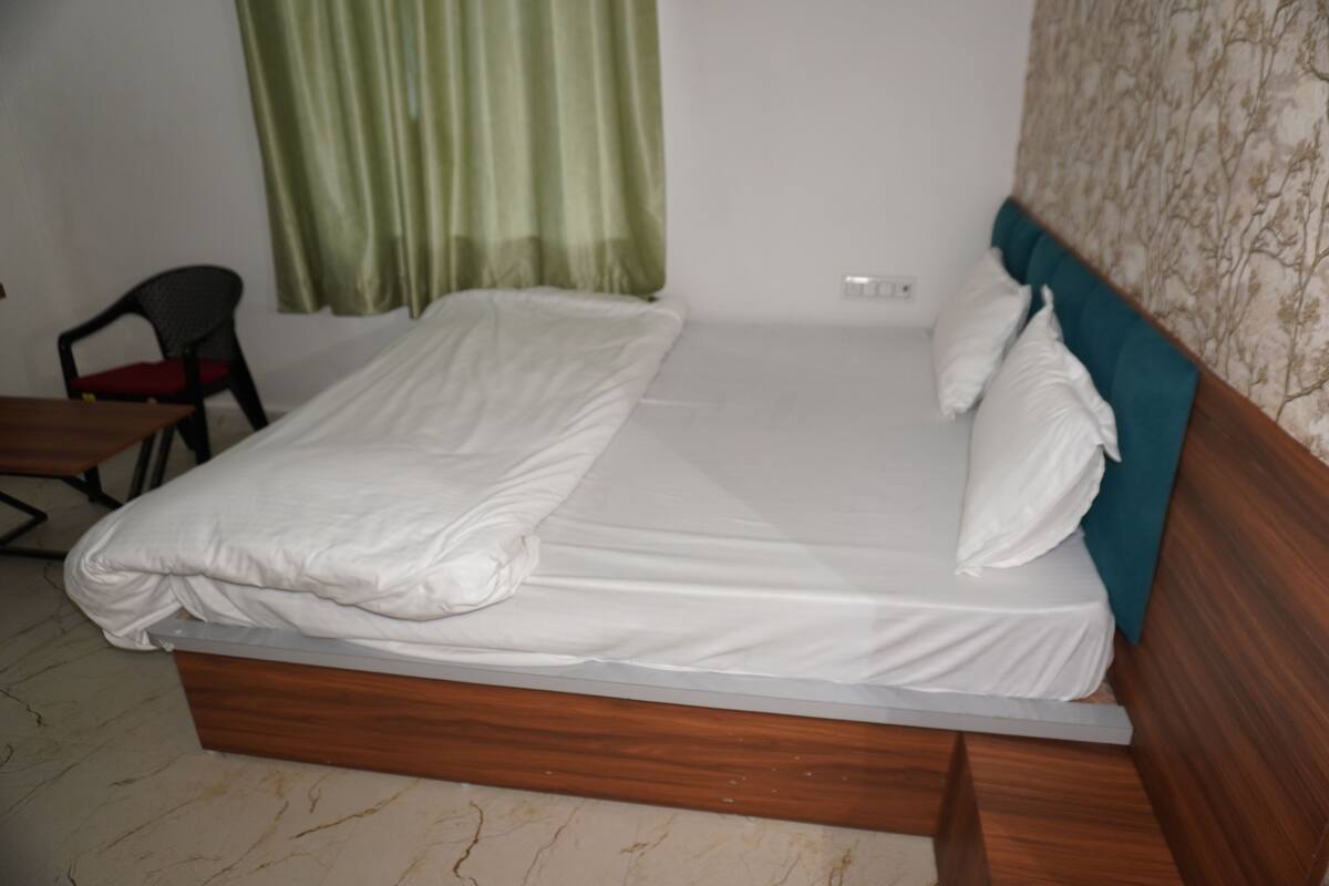 Un llit individual amb estructura de fusta i roba de llit blanca a una habitació amb cortina verda i paret amb dibuixos.