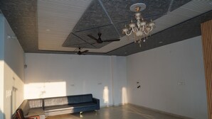 Ein geräumiges Zimmer mit Deckenventilator, einer Chandelüster, einer Couch und einer Holzwand rechts.