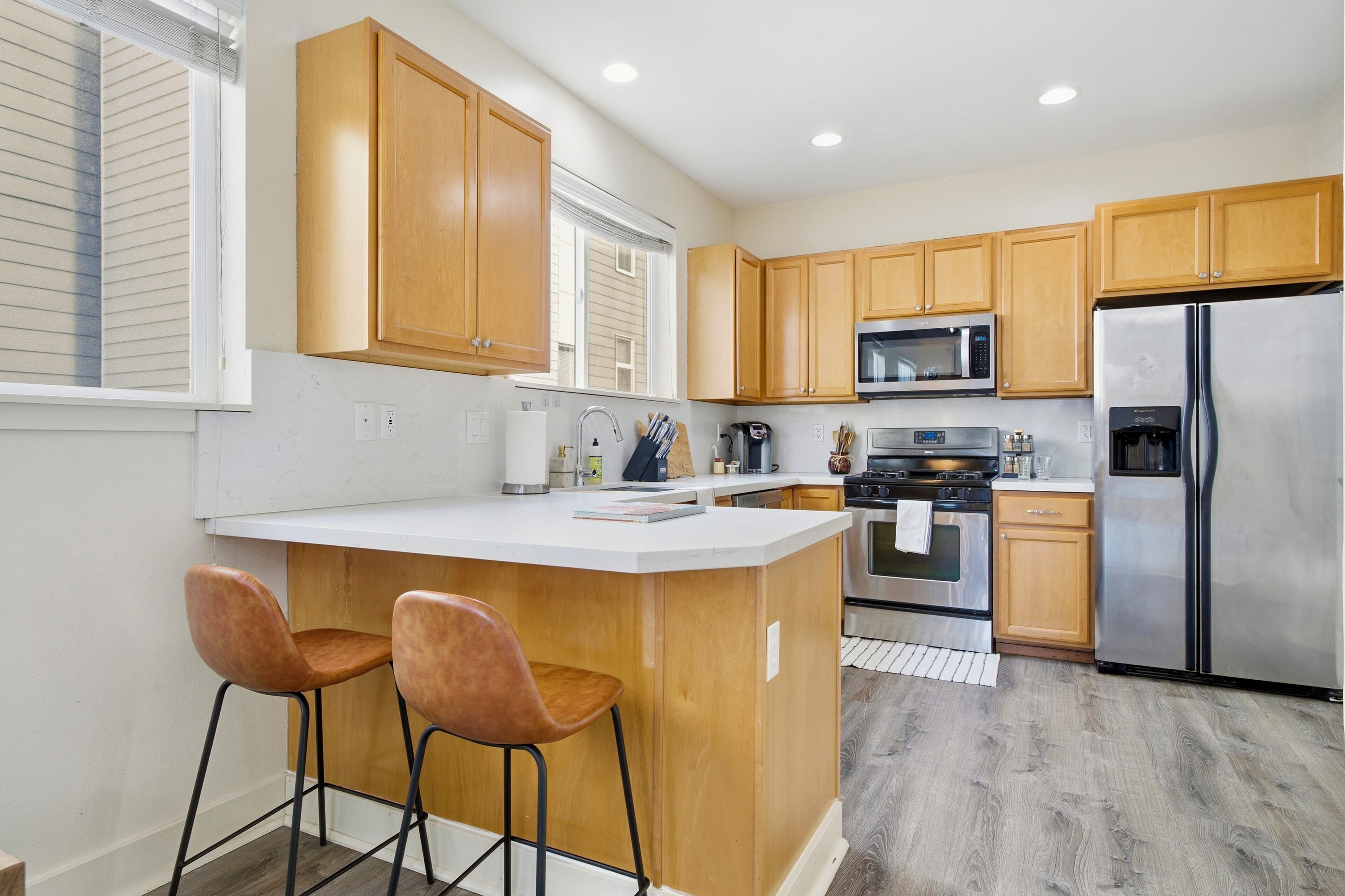 A modern kitchen with wooden cabinets, a stainless steel refrigerator, a microwave, and a large island with two bar stools.
