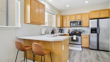 A modern kitchen with wooden cabinets, a stainless steel refrigerator, a microwave, and a large island with two bar stools.
