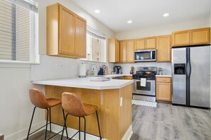 Una cocina moderna con armarios de madera, un refrigerador de acero inoxidable, un microondas y una isla grande con dos taburetes de bar.