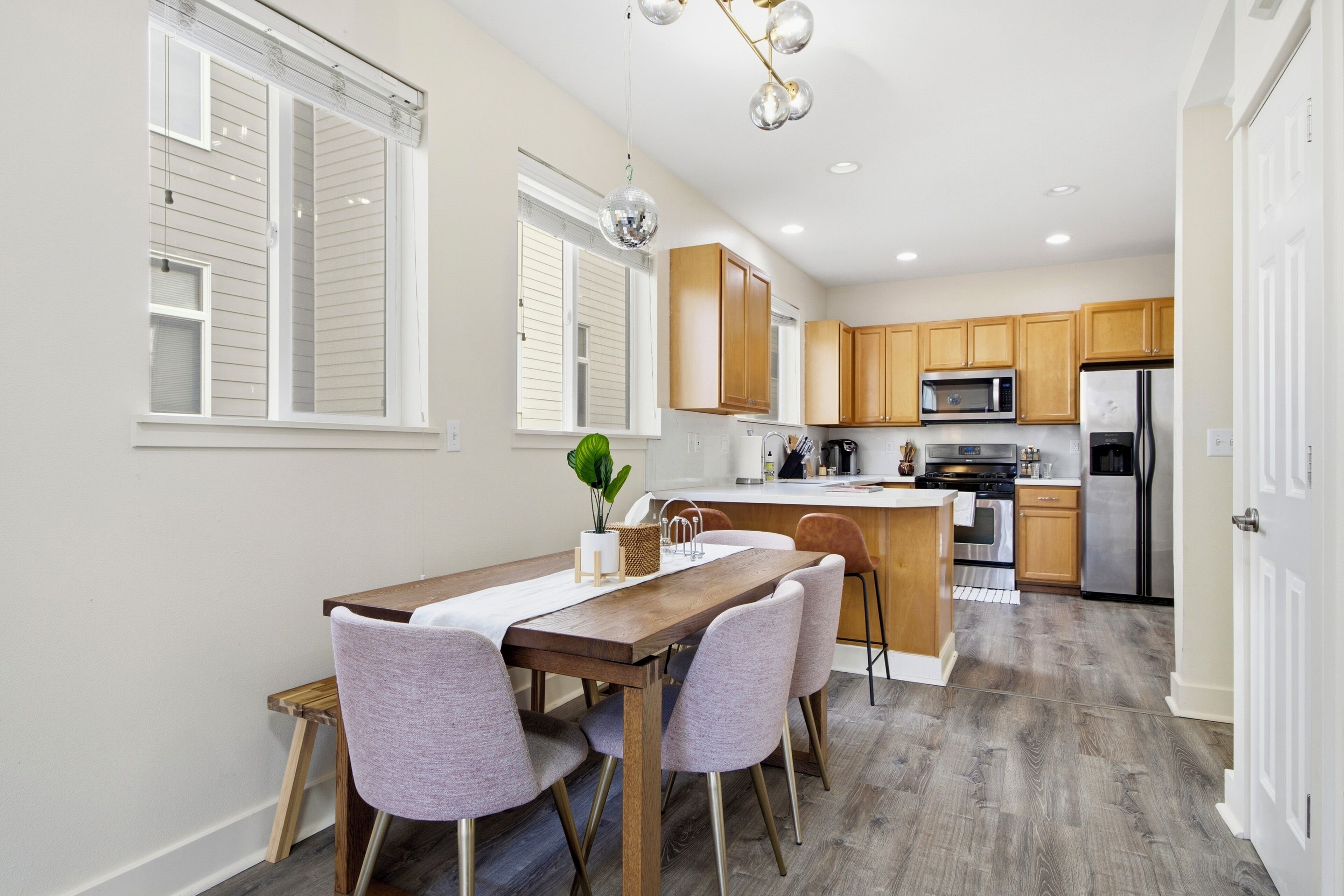 A modern kitchen with wooden cabinets, a stainless steel refrigerator, and a dining area with a wooden table and chairs.
