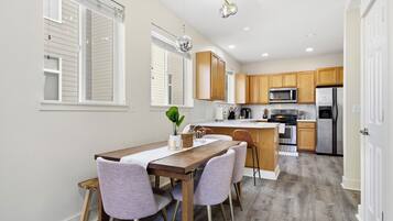 A modern kitchen with wooden cabinets, a stainless steel refrigerator, and a dining area with a wooden table and chairs.