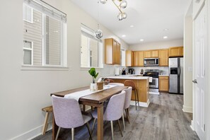 Una cocina moderna con armarios de madera, un refrigerador de acero inoxidable y un comedor con mesa y sillas de madera.