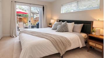 A bedroom with a large bed, a nightstand, a lamp, and a view of the outdoors through a sliding door.