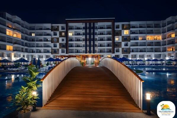 A hotel with a pool, a wooden bridge, and multiple balconies.
