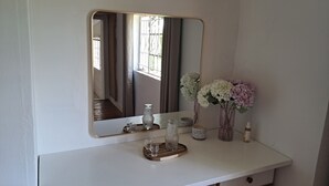 A white vanity with a mirror, a small vase with flowers, and a tray with glasses and a bottle. - Peaceful, quiet, and safe family friendly home (Rosendal)