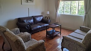 A living room with a leather sofa, patterned armchairs, a wooden coffee table, a lamp, and a window with curtains. - Peaceful, quiet, and safe family friendly home (Rosendal)