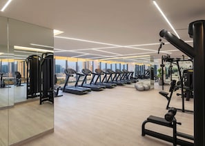 Ett modernt gym med löpband, styrketräningsmaskiner och en stor spegel som reflekterar stadens silhuett.