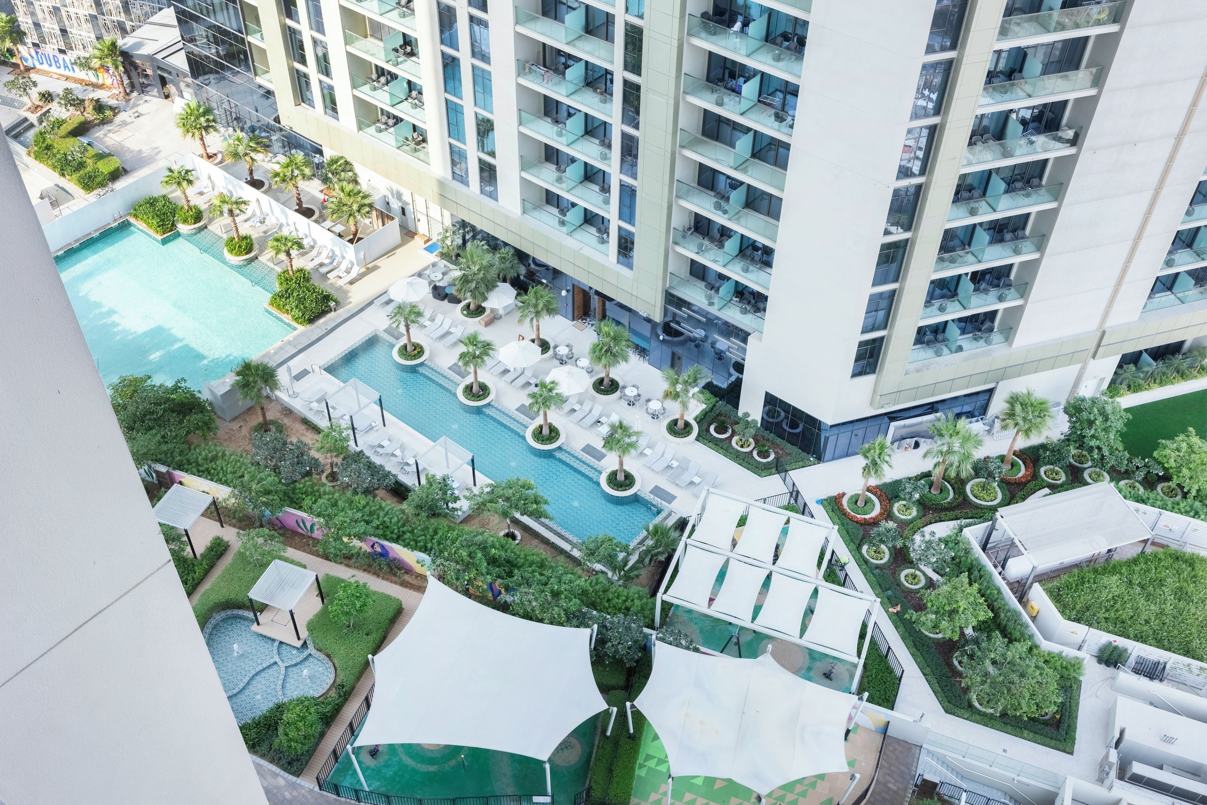A high-rise hotel with multiple balconies, a central swimming pool, and surrounding greenery.