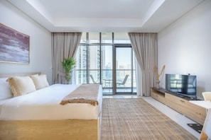 Ein modernes Hotelzimmer mit einem großen Bett, einem Flachbildfernseher, einem Schreibtisch und Blick auf die Stadt durch raumhohe Fenster.