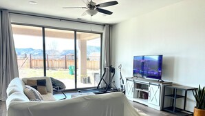 A living room with a covered sofa, a TV on a stand, and a sliding glass door leading to a backyard. - Quiet place (Spanish Springs)