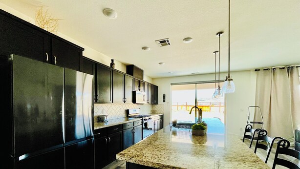 A modern kitchen with dark cabinetry, a granite countertop, and a central island. - Quiet place (Spanish Springs)