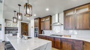 A modern kitchen with a large island, wooden cabinets, and pendant lighting. - 5 Mi to Flathead River: Serene Mountain-View Gem! (Columbia Falls)
