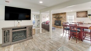 Een moderne woonkamer met een flatscreen televisie, open haard, eethoek en een keuken op de achtergrond.