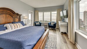 Ein Schlafzimmer mit einem großen Bett, einem Deckenventilator, einem Schreibtisch mit Fernseher und Blick auf die Stadt.
