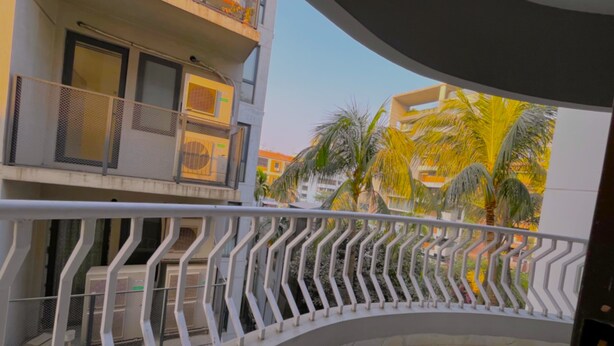 Ein gebogener Balkon mit Metallgeländer, der auf einen Wohnbereich mit Palmen und Gebäuden blickt.
