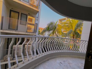 Ein gebogener Balkon mit Metallgeländer, der auf einen Wohnbereich mit Palmen und Gebäuden blickt.