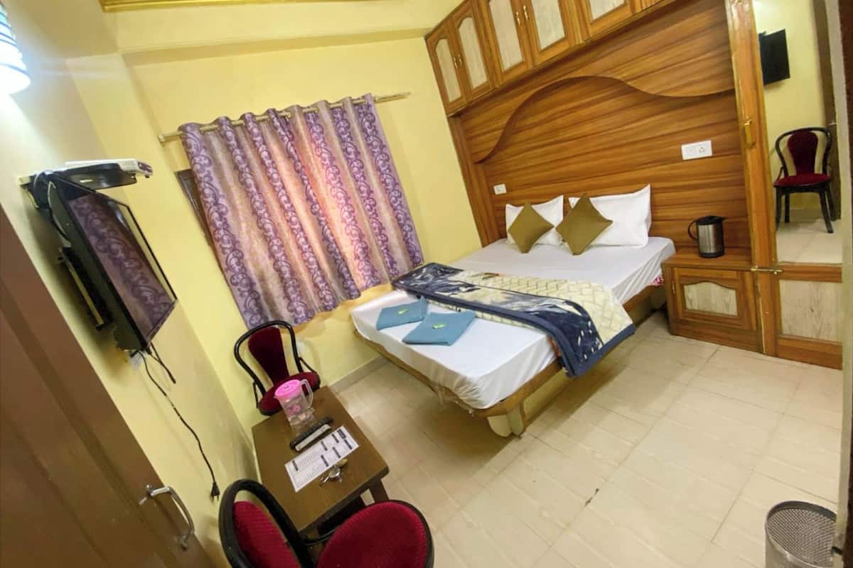 Un dormitorio con cabecera de madera, cama con manta estampada, escritorio con silla y televisor en la pared.