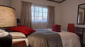 Une chambre d’hôtel avec un lit, un bureau, une lampe, une chaise et une fenêtre avec des rideaux.