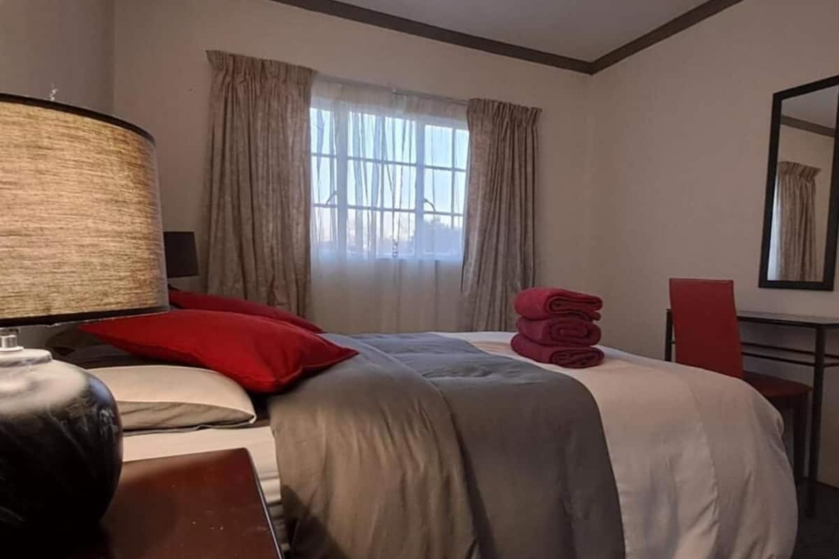 A hotel room with a bed, a desk, a lamp, a chair, and a window with curtains.