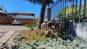 Un espace de stationnement avec une voiture blanche, un abri-voiture et un jardin agrémenté de plantes succulentes et d’une mangeoire à oiseaux.