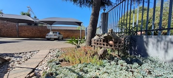 Un aparcamiento con un coche blanco, un garaje cubierto y un jardín con suculentas y un comedero para pájaros.