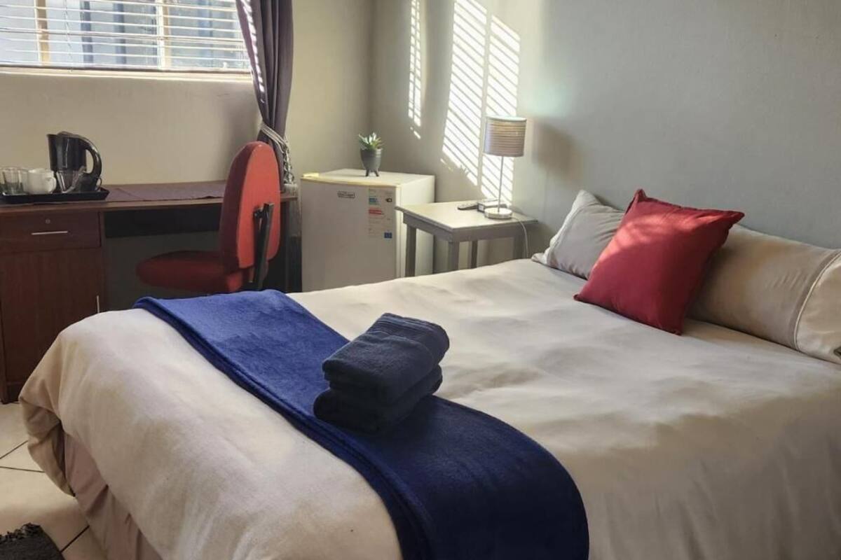 A hotel room with a bed, a desk, a chair, a small table, and a window with curtains.