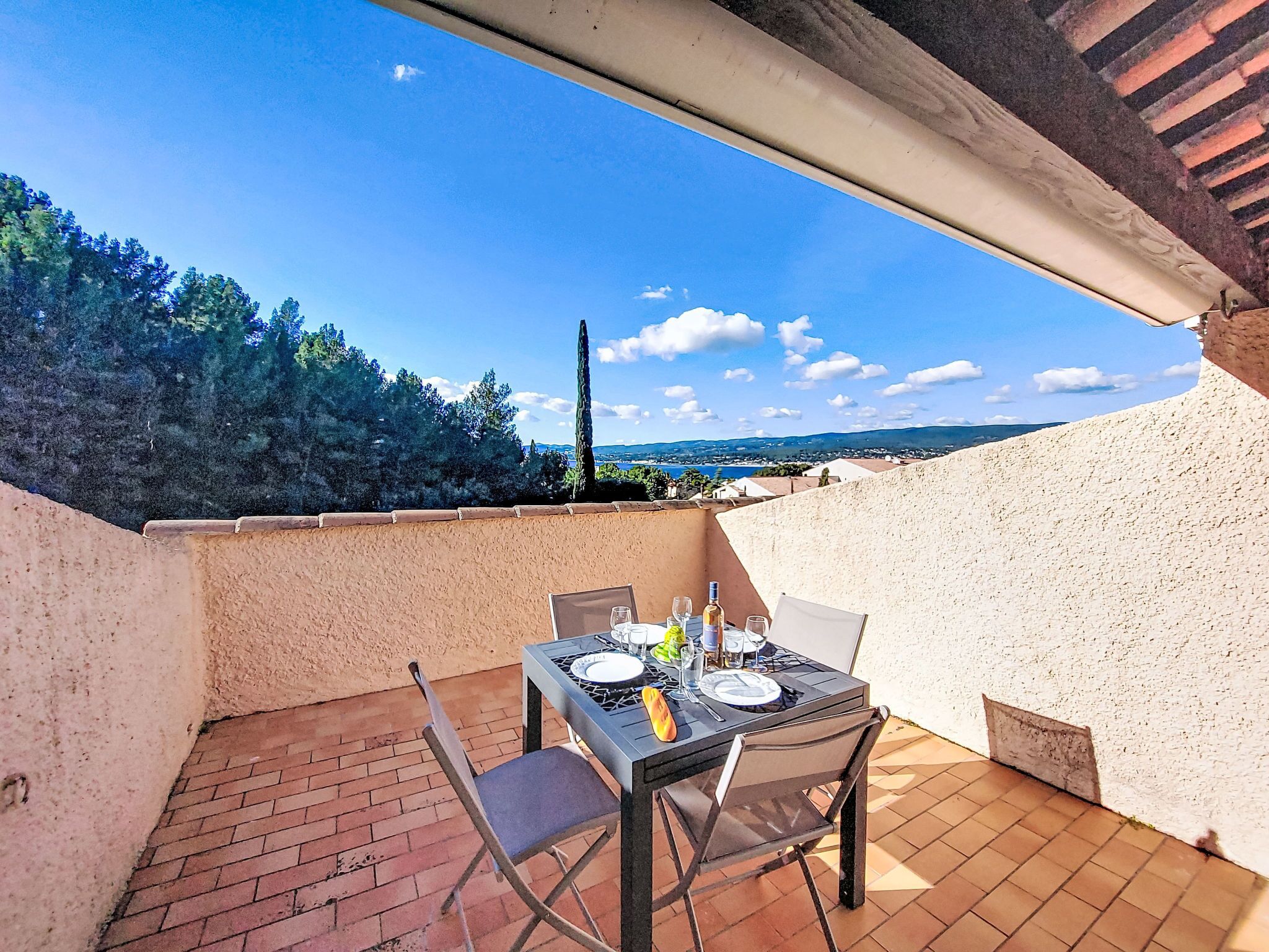 Eine Terrasse mit Tisch für zwei Personen, mit Blick auf eine malerische Landschaft, Bäume und eine ferne Meeransicht.