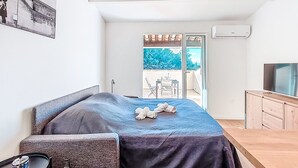 Ein Schlafzimmer mit Bett, kleinem Tisch, Fernseher und einem Balkon mit Blick auf Bäume.