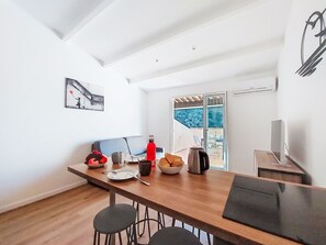 A modern kitchen with a wooden countertop, bar stools, and a dining table. There is a window with a view of greenery outside. - Hauts de la Madrague by Interhome (Saint Cyr sur Mer La Madrague)