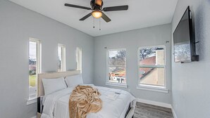 Une chambre à coucher avec un lit, un ventilateur de plafond, des fenêtres et un téléviseur.