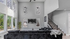 Un salon moderne avec un grand canapé d’angle, un escalier et de grandes fenêtres.