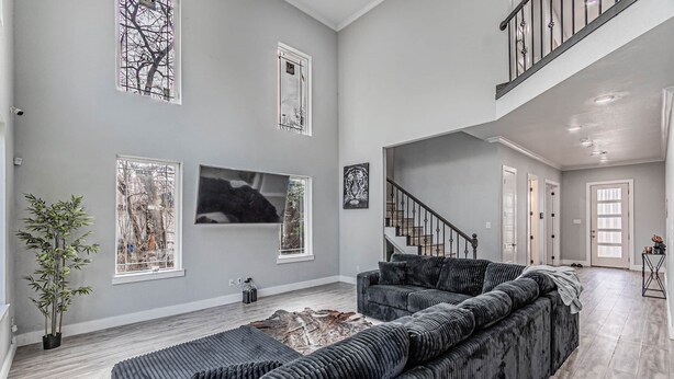 Un salon spacieux avec un grand canapé d’angle, un escalier et une grande fenêtre donnant sur les arbres.